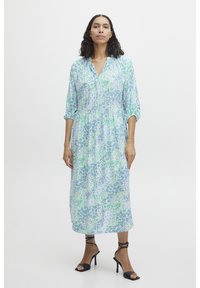 Vestido floral en tonos azul claro y verde, con cuello tipo solapa, mangas de tres cuartos y una silueta en capas. Tacones negros con tiras.