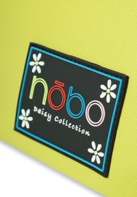 Gelbes strukturiertes Material mit einem schwarzen Markenabzeichen, das bunte Buchstaben und kleine weiße Blumen zeigt, beschriftet mit "Daisy Collection."