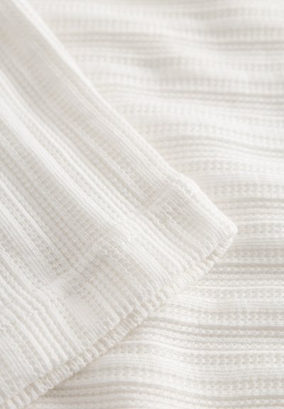 Hvitt teksturert stoff med horisontale striper og rillet mønster, som viser et mykt og lett utseende.