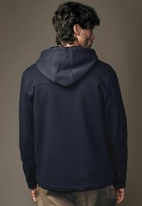 Navy hooded sweatshirt with textured fabric, ribbed details on shoulders, and a relaxed fit. Features a split hem and cuffs.