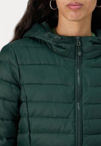 Mørkegrønn puffjakke med glidelås, hette-design og horisontal quiltet tekstur. Inkluderer snordetaljer nær hetten.