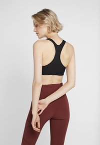 Svart sportsbh med teksturert design, med racerback-kutt, kombinert med høy midje burgunder tights. Enkel og funksjonell stil.
