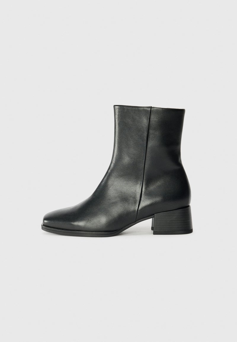 Botas de cuero negro hasta el tobillo con textura suave, puntera redondeada y tacón cuadrado. El diseño presenta una silueta simple y elegante.