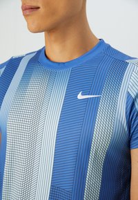 Blue athletic T-shirt featuring a geometric pattern with varying lines and shades, round neckline, and a white Nike logo on the chest.