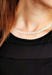 Collier de perles blanches avec une texture lisse et ronde, présentant des perles uniformément espacées, porté sur un haut noir. Design simple et élégant.