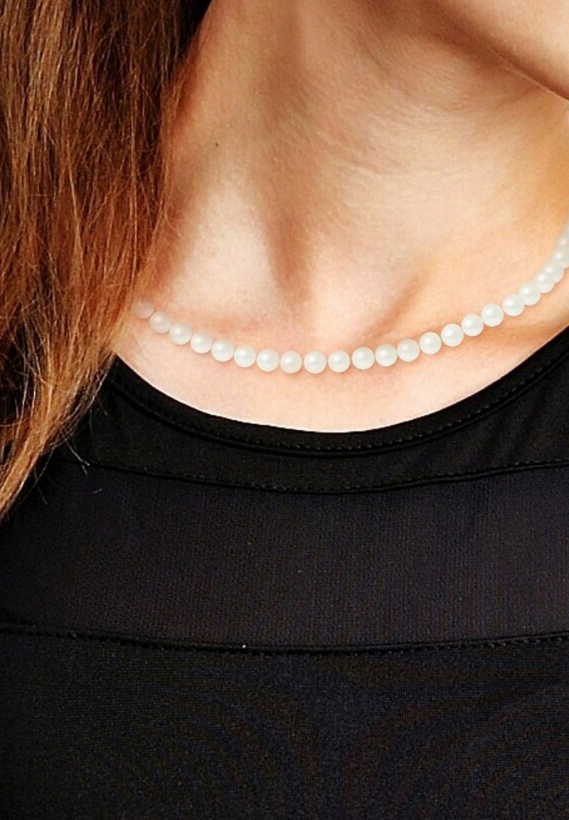 Collier de perles blanches avec une texture lisse et ronde, présentant des perles uniformément espacées, porté sur un haut noir. Design simple et élégant.
