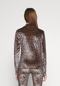 Top lungo a maniche con stampa leopardata in tessuto metallico, design aderente, alta brillantezza, audace motivo marrone e nero, texture elegante, abbinato a pantaloni simili.
