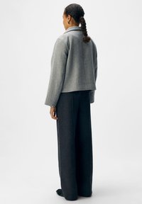 Grau melierte Wollmischjacke mit maßgeschneidertem Design, lockerer Passform und Reverskragen, kombiniert mit dunklen, weiten Hosen.