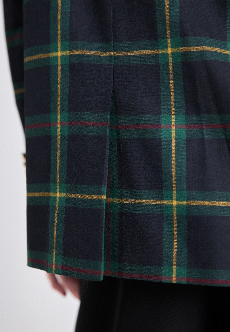 Blazer en mélange de laine avec un fond bleu marine foncé orné d'un motif à carreaux verts, jaunes et bordeaux, et doté d'une fente latérale.