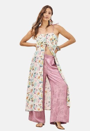 Vestido sin mangas con estampado floral y abertura frontal sobre pantalones de pierna ancha rosas. La tela parece ligera y texturizada. Accesorios simples.