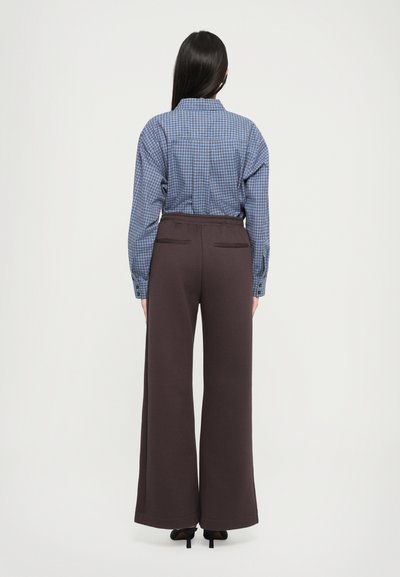 Μπλε καρό πουκάμισο με κουμπιά και μακριά μανίκια, συνδυασμένο με φαρδιές καφέ παντελόνες. Οι παντελόνες έχουν λεία υφή και ελαστική μέση.