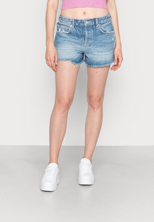 Shorts en denim bleu clair, avec un ourlet effiloché, cinq poches et un design légèrement usé, associés à des baskets blanches.