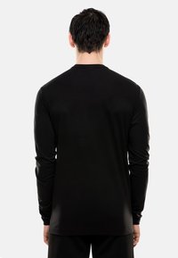 T-shirt nera a maniche lunghe, realizzata in tessuto morbido, presenta un collo rotondo e un orlo dritto. Texture liscia, design minimale, senza loghi visibili.