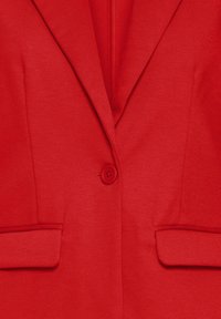 Blazer rouge avec un seul bouton rouge, revers crantés et deux poches avant à rabat, en tissu texturé.