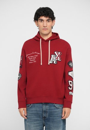 Maroone hoodie med snøre, prydet med forskellige farverige lapper og tekst på fronten og ærmerne. Lavet af blødt stof, afslappet pasform.
