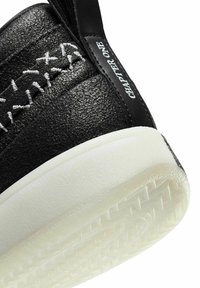 Baskets noires avec une tige texturée, des détails de coutures blanches, et une semelle épaisse en caoutchouc blanc avec une bande de roulement à motifs.