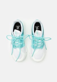 Ett par vita och ljusblå löparskor med snörningen knuten, sedd ovanifrån på en vit bakgrund.