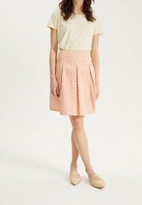 Camiseta amarilla clara de manga corta con texto bordado, combinada con una falda rosa plisada con un patrón geométrico. Alpargatas de yute beige.