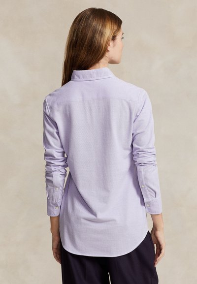 Light purple button-up shirt with long sleeves, a collar, and a rounded hem. Fabric has a textured weave and features white button details.