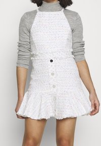 Bílá tvídová šaty se zvonov ým lemem, s texturovanou vazbou a pastelovými akcenty. Přední knoflíky a úzký pas vytvářejí strukturu.