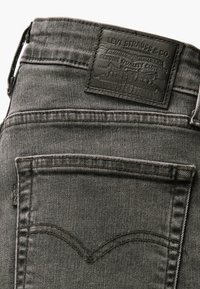 Zone de la poche arrière d'un jean Levi Strauss gris foncé avec un patch en cuir de la marque et des détails de couture sur la poche.