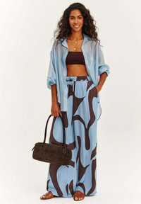 Svetlomodrá priesvitná košeľa s gombíkmi cez hnedý crop top, doplnená širokými nohavicami s hnedým abstraktným vzorom. Hnedá kabelka.