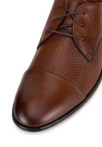 Hnedé kožené topánky s textúrovaným tkaným vzorom na vrchu, hladkým špičkovým dielom a tmavohnedými šnúrkami. Ploché gumové podrážky.