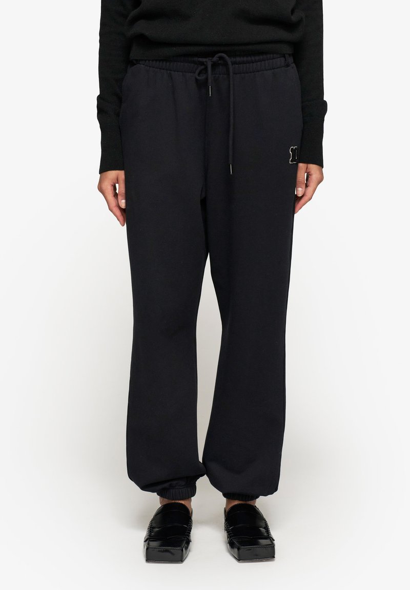 Czarne dresy z elastycznym paskiem w talii, sznurkiem i ściągaczami u dołu nogawek. Zawierają małe wyszywane logo na lewym biodrze.