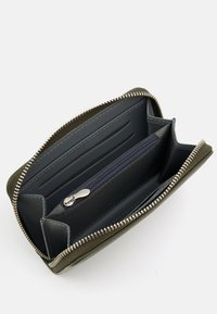 Compact zip wallet in olive green with a textured exterior. Features a navy interior, card slots, and a zippered coin compartment. Silver hardware.