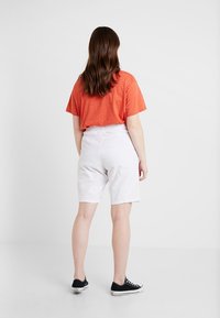 Chemise rouge à manches courtes, shorts blancs jusqu'aux genoux et baskets noires. Coupe droite et tissu léger. Design simple, sans motifs.