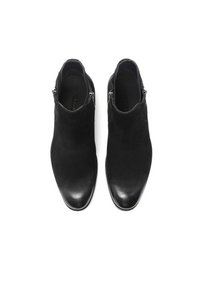 Botas negras de tobillo de ante con puntera de cuero liso. Cuentan con cremalleras laterales y una forma estilizada. Parte superior texturizada con acabado mate.