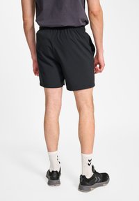 Svarta shorts med elastisk midja och sidofickor, tillverkade av lätt material, visade upp på en person som bär svarta skor och vita strumpor.