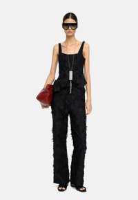 Czarny, teksturowany strój z bluzką peplum, szerokimi spodniami, dużymi okularami przeciwsłonecznymi, srebrną naszyjnikową zawieszką i czerwoną torebką. Gładka, skomplikowana tkanina.