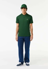 Donkergroen poloshirt met een kraag en korte mouwen, gecombineerd met blauwe spijkerbroeken en donkerblauwe sneakers. Eenvoudig ontwerp zonder patronen.