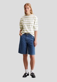 Gestreepte langemouw shirt in lichtgroen en wit, gecombineerd met blauwe denim bermuda shorts. Draag het met zwarte schoenen en witte sokken.