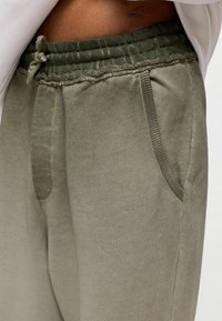 Olijfgroene sweatpants met een elastische tailleband, trekkoorddetails en zijzakken; zachte textuur met subtiele stiksels.