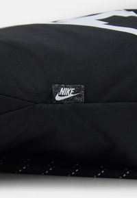 Svart tyg med en slät yta som har en Nike-logopatch, geometrisk design och ett sömnadsmönster på den nedre delen.