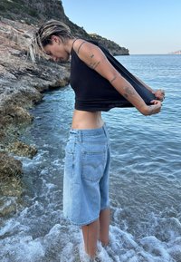 Calções de ganga em lavagem azul clara, com bainha desfiada e bolsos traseiros clássicos; combinados com uma t-shirt preta justa num ambiente natural.