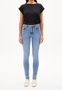 Úzké džíny ve světle modrém denimu, s vysokým pasem, pěti kapsami a poutky na pásek, kombinované s černým krátkým rukávem a bílými nazouvacími botami.