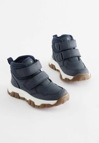 Marinblå mid-cut sneakers med två kardborreband, vit mellansula och brunt gummisul. Har en texturerad yta och vadderad krage.