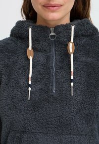 Šedý fleece svetr s límcem na zip, zdobený smetanovými šňůrkami, koženými detaily a měkkým, strukturovaným povrchem.