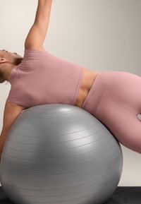 Ținută sport roz cu dungi, purtată de o persoană întinsă pe o minge de exerciții gri. Mingea are o textură netedă cu nervuri orizontale.