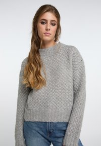 Maglione lavorato a maglia grigio chiaro con un motivo a diamante testurizzato, scollo rotondo e orlo a costine, abbinato a jeans blu. Design accogliente e aderente.