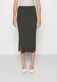 Knit, ribbed midi skirt in dark green with a side slit, paired with pointed white heels. Smooth texture and fitted design.