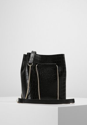 Sac seau en cuir noir embossé crocodile avec détails de fermeture éclair dorés et bandoulière détachable sur une surface blanche.