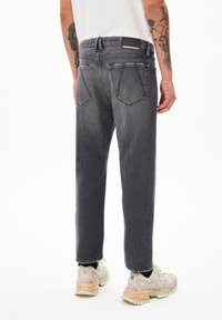 Schwarze Jeans mit lockerer Passform, hoher Taille, Gesäßtaschen und einem Logo-Patch am Bund. Kombiniert mit gemusterten Sneakers.