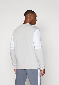 Sweat-shirt gris avec des panneaux blancs, col rond et poignets côtelés. Design minimaliste avec une texture lisse et sans motifs visibles.