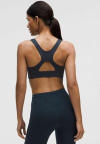 Sujeción deportiva negra con un corte triangular en la parte posterior, tirantes anchos, textura suave, combinada con leggings de cintura alta a juego.
