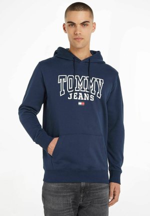 Felpa blu navy con tasca frontale tipo kangaroo, con testo bianco "TOMMY JEANS" e un piccolo accento logo rosso e bianco. Materiale cotone.