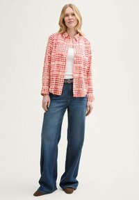 Gemusterte rosa Hemdbluse aus leichtem Stoff, kombiniert mit weit geschnittenen blauen Denim-Jeans. Das Outfit hat ein weißes Tanktop darunter.